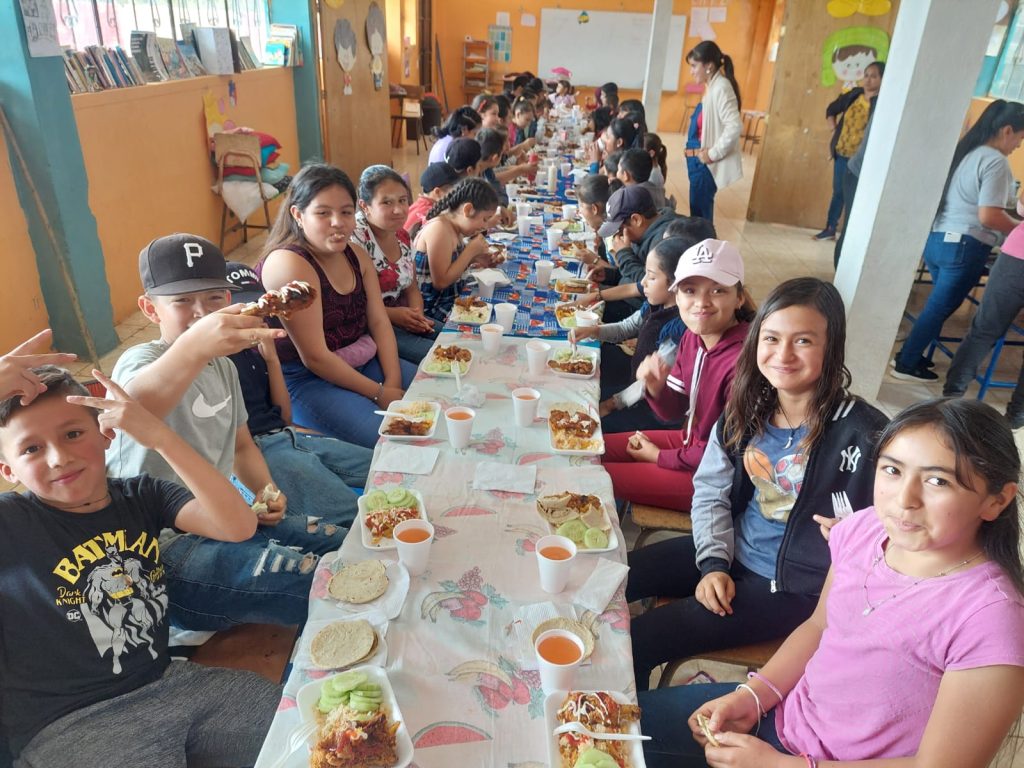 Children of Escuela Primaria Aldea El Socorro sharing a meal at a long table